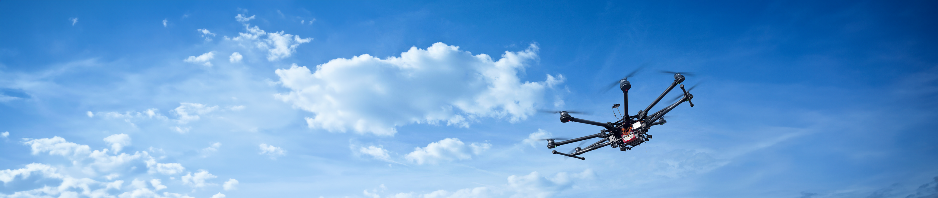 A drone flying in a clear blue sky with scattered clouds, showcasing advanced aerial technology and high-altitude capabilities.