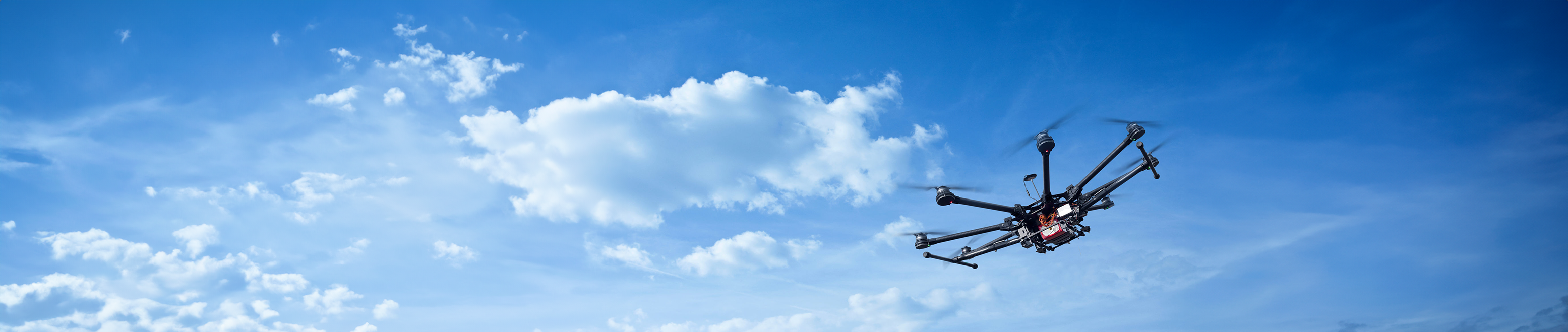  A drone flying in a clear blue sky with scattered clouds, showcasing advanced aerial technology and high-altitude capabilities.